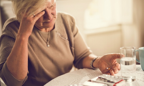 An older woman taking tablets and looking confused