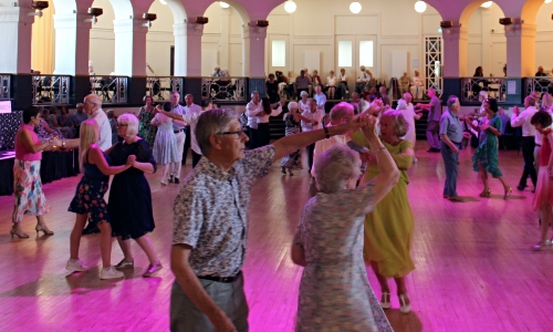 A large group of older people dancing in a grand 1920s ballroom