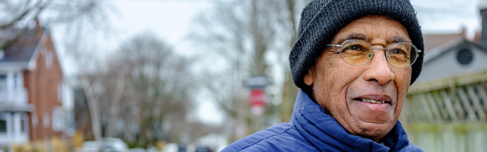 An older Black man in a beanie, standing outside and looking cold